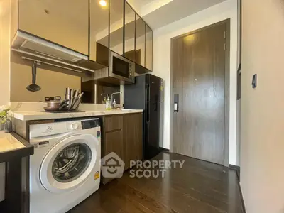 Modern kitchen with washing machine, microwave, and sleek cabinetry in compact apartment.