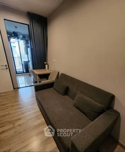 Cozy living room with modern sofa and wooden flooring, leading to a bright balcony view.