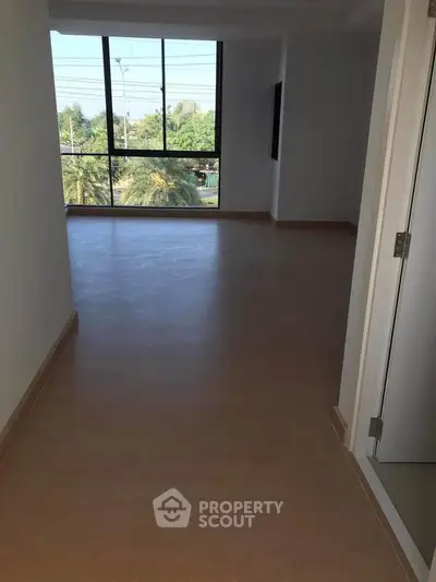 Spacious empty room with large window offering lush green view, perfect for customization.