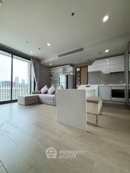 Modern open-plan living room with kitchen and city view, featuring sleek furniture and large windows.