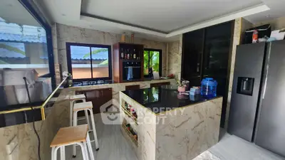 Modern kitchen with marble countertops and island, featuring large windows and stainless steel appliances.