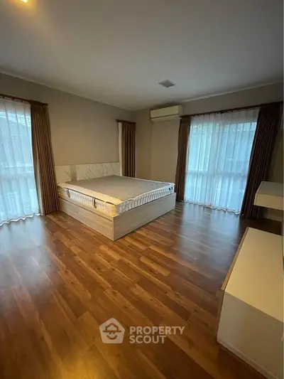 Spacious bedroom with wooden flooring and large windows for natural light