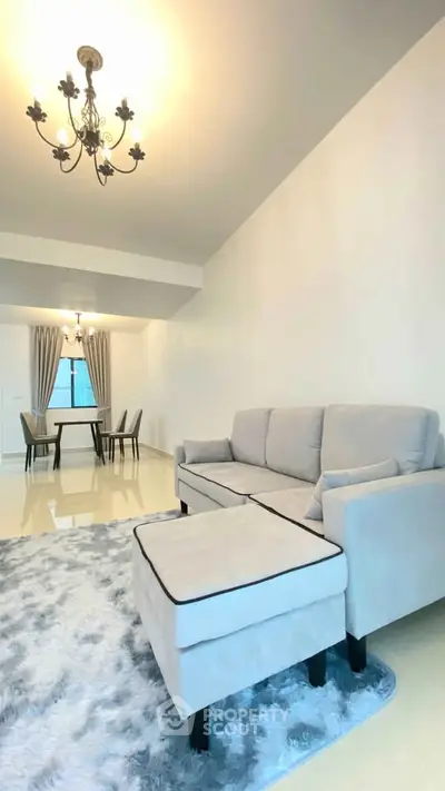 Elegant living room with plush sofa and dining area, featuring modern chandeliers and cozy ambiance.