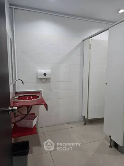 Modern bathroom with red sink and white tiled walls in a commercial building.