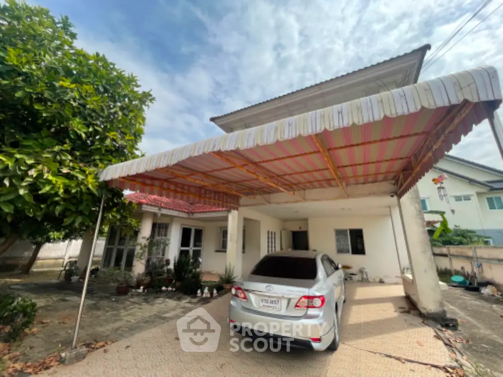 Spacious family home with covered carport and lush greenery, featuring a large driveway and a welcoming entrance.