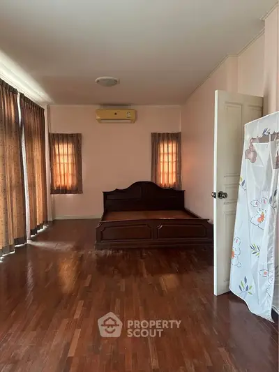 Spacious bedroom with wooden flooring and large windows for natural light
