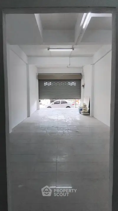 Spacious empty garage with tiled flooring and roll-up door, ideal for storage or parking.