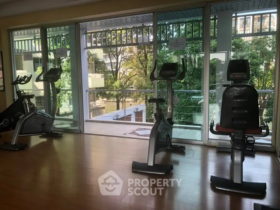 Modern gym with exercise bikes and large windows overlooking lush greenery.