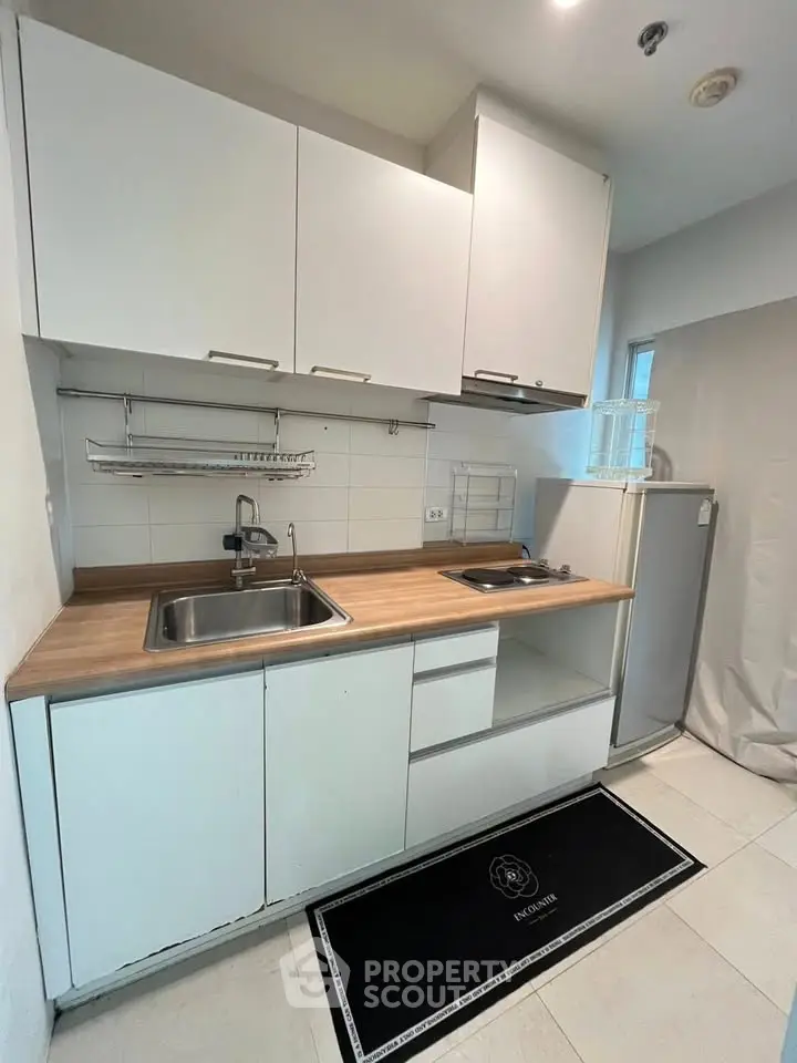 Modern compact kitchen with sleek white cabinets and wood countertop, featuring a small fridge and electric stove.