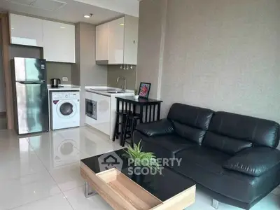 Modern living room with sleek kitchen, black leather sofa, and stainless steel appliances.