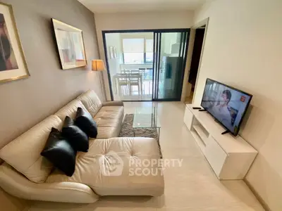 Modern living room with stylish sofa and TV, leading to a bright dining area with balcony view.
