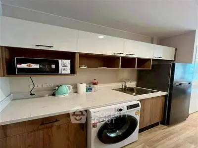Modern kitchen with washing machine, microwave, and fridge in compact layout.