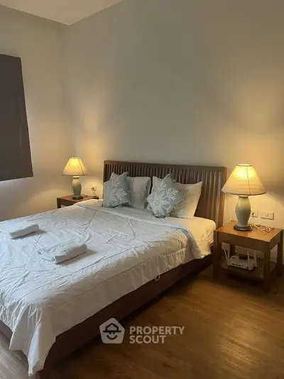Cozy bedroom with wooden flooring and elegant bedside lamps, perfect for relaxation.
