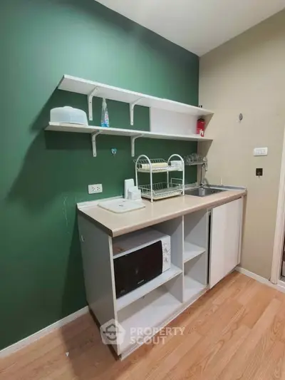Compact kitchen with green accent wall, open shelving, and microwave in modern apartment.