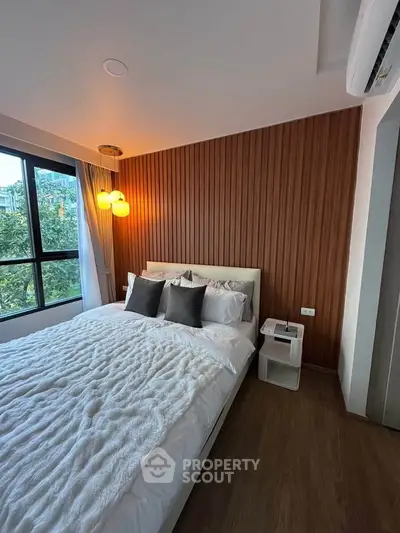 Cozy bedroom with wooden accent wall and large window offering a serene view, perfect for relaxation.