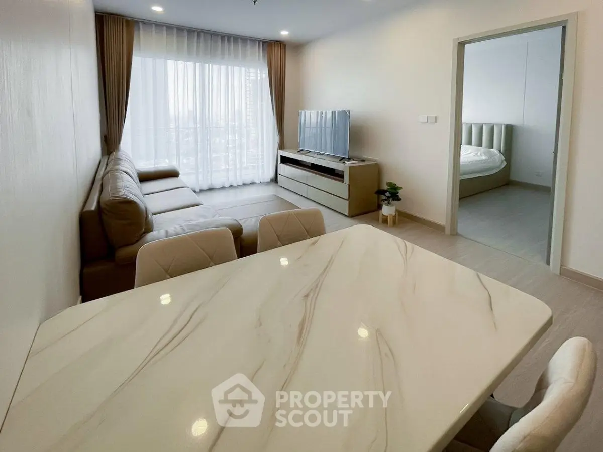 Modern living room with elegant marble dining table and cozy seating area, featuring a large window for natural light.