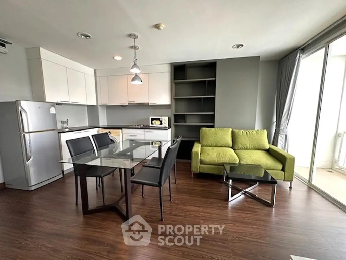 Modern living room with open kitchen, glass dining table, and green sofa in a bright apartment.