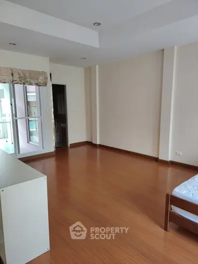 Spacious bedroom with wooden flooring and balcony access in modern apartment.