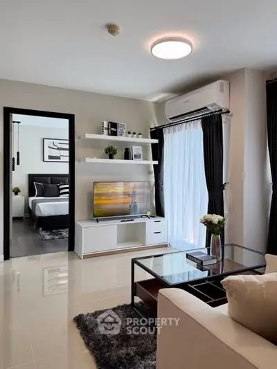 Modern living room with sleek furniture and large window, leading to a stylish bedroom.