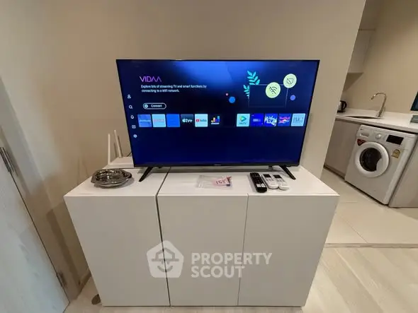 Modern living room with sleek TV setup and compact kitchen featuring washing machine.