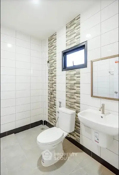 Modern bathroom with sleek white tiles and stylish accents, featuring a toilet and sink.
