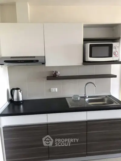 Modern kitchen with sleek cabinetry, microwave, and electric kettle in a compact layout.