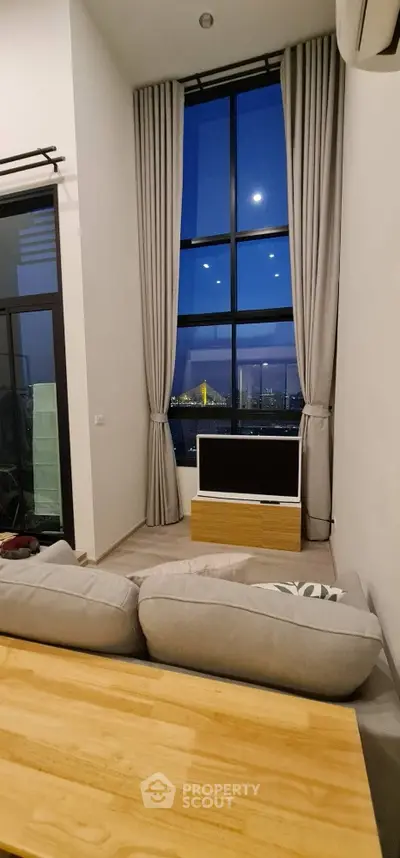 Modern living room with high ceiling and stunning city view through large windows.
