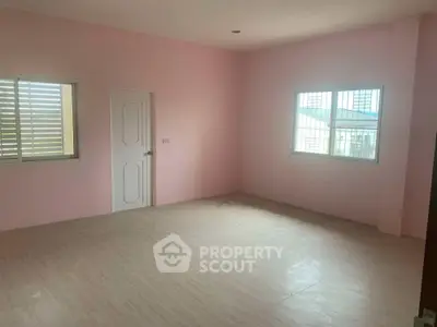 Spacious empty room with pink walls and tiled flooring, featuring two windows for natural light.
