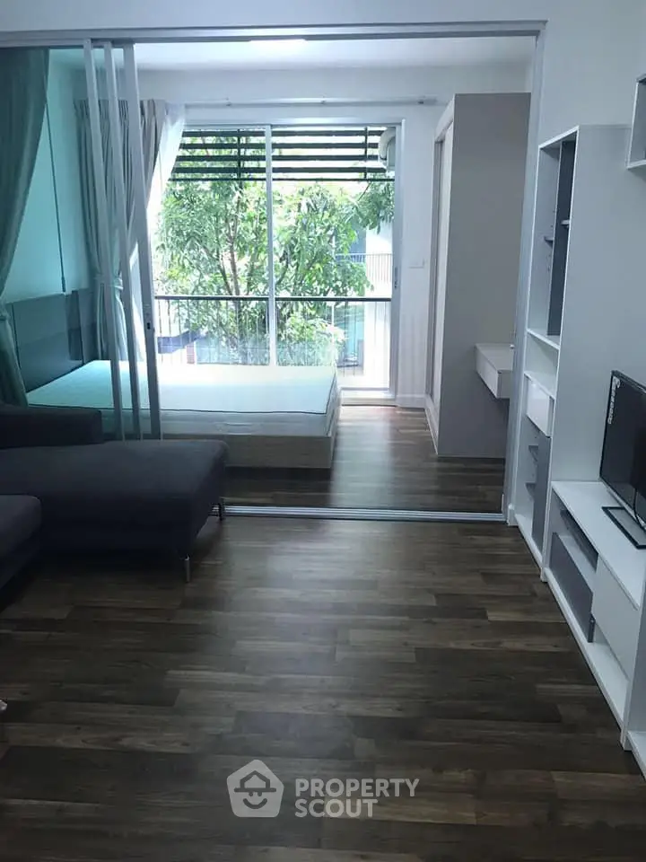Modern apartment with sliding glass doors, hardwood floors, and a view of lush greenery.