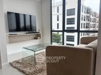 Modern living room with large windows and city view, featuring a sleek TV setup and cozy seating area.