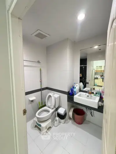 Compact bathroom with modern fixtures and white tiles, featuring a toilet, sink, and mirror.