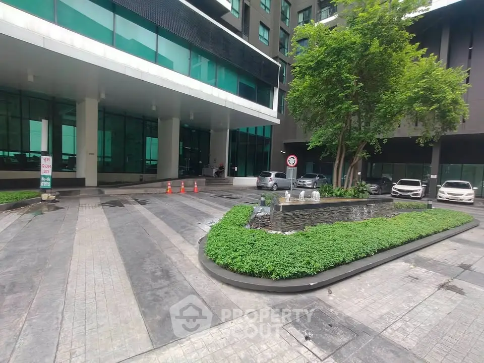 Modern building entrance with lush greenery and parked cars, showcasing urban living convenience.