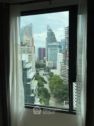 Stunning cityscape view from a high-rise apartment window, showcasing modern architecture and lush greenery.