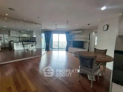 Spacious living room with wooden flooring and mirrored wall, open to modern kitchen.