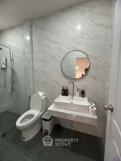 Modern bathroom with sleek design, featuring a round mirror, white sink, and glass shower enclosure.