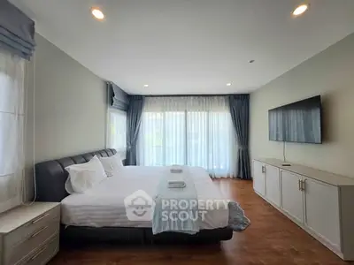 Spacious bedroom with modern decor, large windows, and a wall-mounted TV, perfect for relaxation.