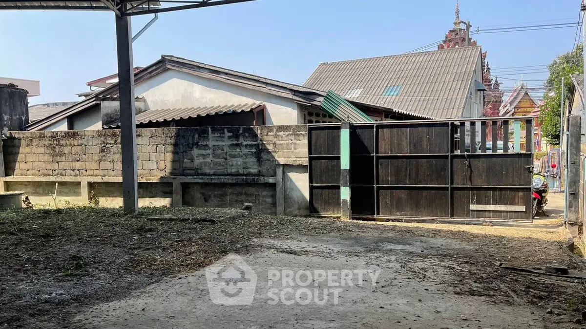 Spacious outdoor area with gated entrance and neighboring buildings in view.