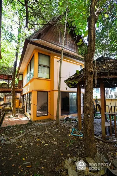 Charming two-story house with lush garden and wooden gazebo, perfect for nature lovers.