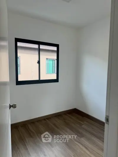 Minimalist small room with wooden flooring and a window, perfect for a cozy study or storage space.