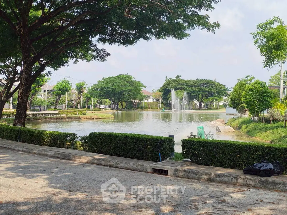 Serene residential lake view with lush greenery and fountain, perfect for tranquil living.