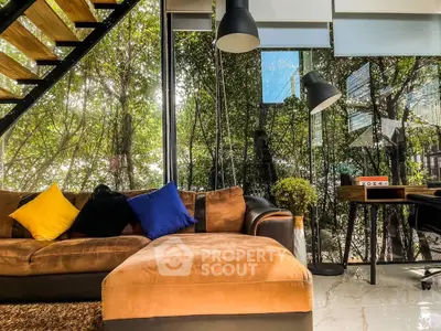 Modern living room with large windows and stylish furniture, featuring a cozy sofa and lush greenery view.