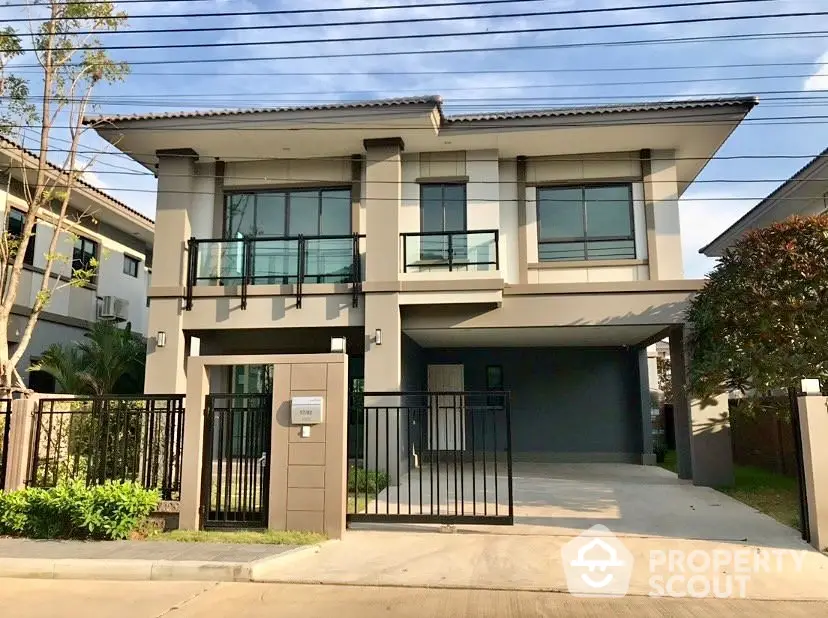 Modern two-story house with large windows and gated driveway in suburban neighborhood.