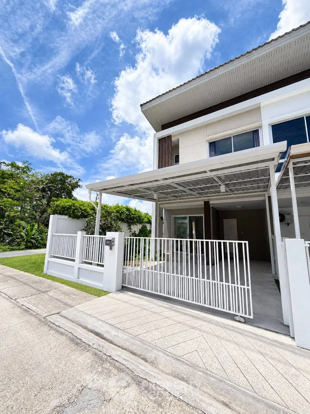 Modern townhouse exterior with gated driveway and lush greenery under a bright blue sky.