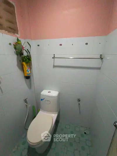Compact bathroom with white tiles and pink walls, featuring a toilet and wall-mounted plant decor.
