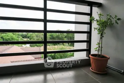 Charming balcony with potted plant and scenic view of lush greenery and rooftops.
