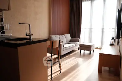 Modern living room with natural light, cozy sofa, and sleek kitchen area in open layout apartment.