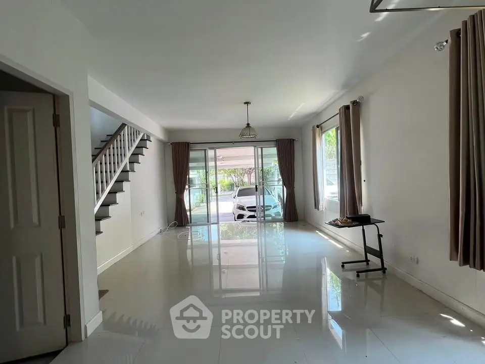 Spacious living room with modern staircase and large windows overlooking driveway.