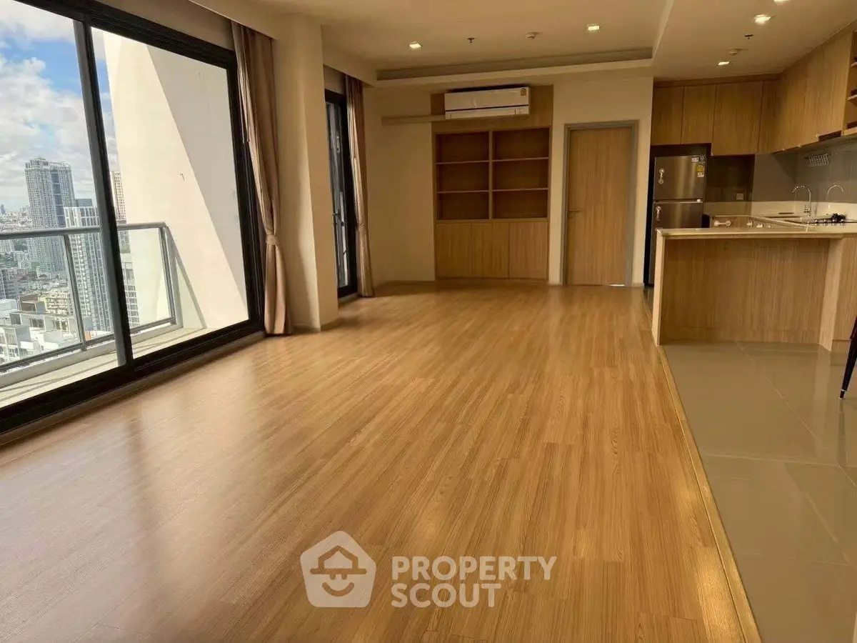 Spacious modern living room with open kitchen and city view balcony in high-rise apartment.