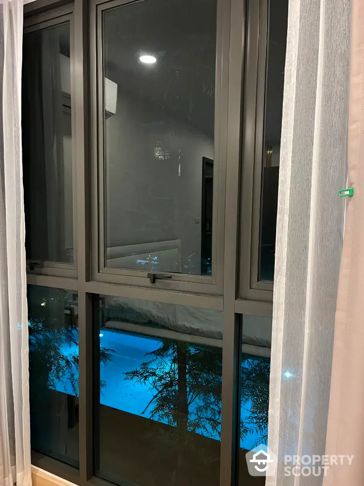 Modern window view overlooking a serene pool at night