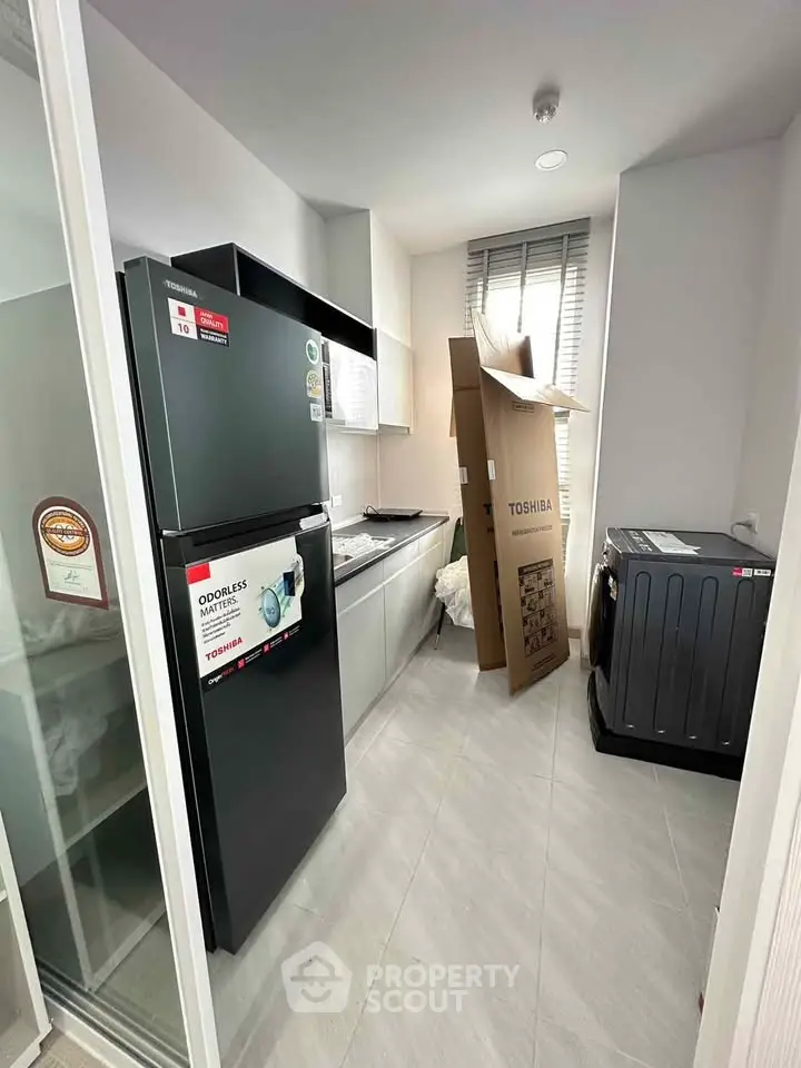 Modern kitchen with sleek appliances and ample natural light, featuring a fridge and washing machine.